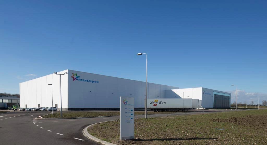 A large industrial building labeled "FrieslandCampina" with a parked truck in front.