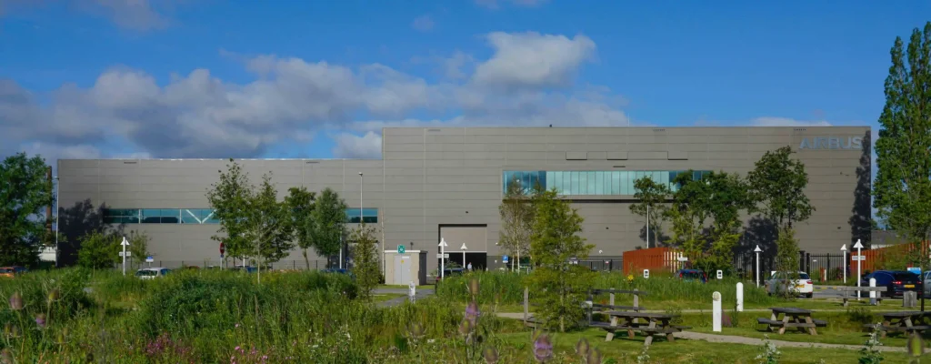 Modern industrial building surrounded by greenery under a blue sky, labeled "Airbus."