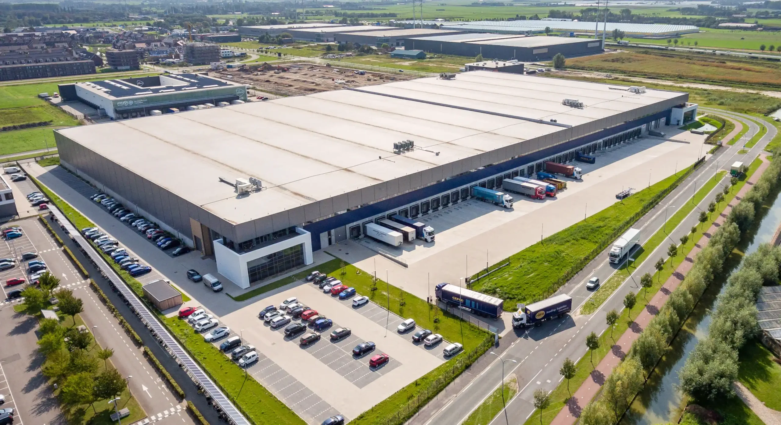 Aerial view of a large warehouse with multiple loading docks, trucks, and a surrounding parking area.