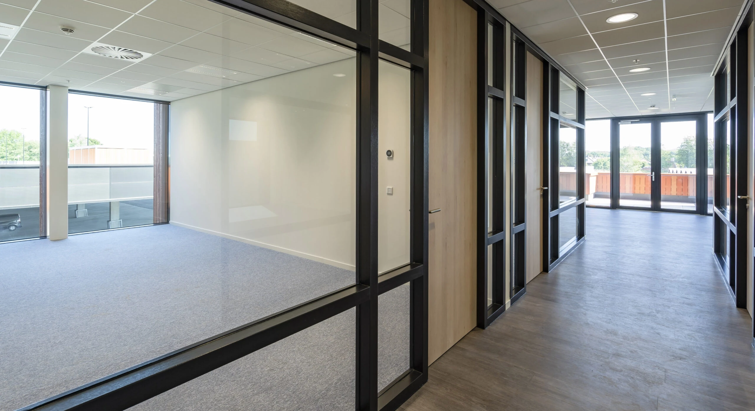 Modern office corridor with glass walls and a view to an adjoining room.