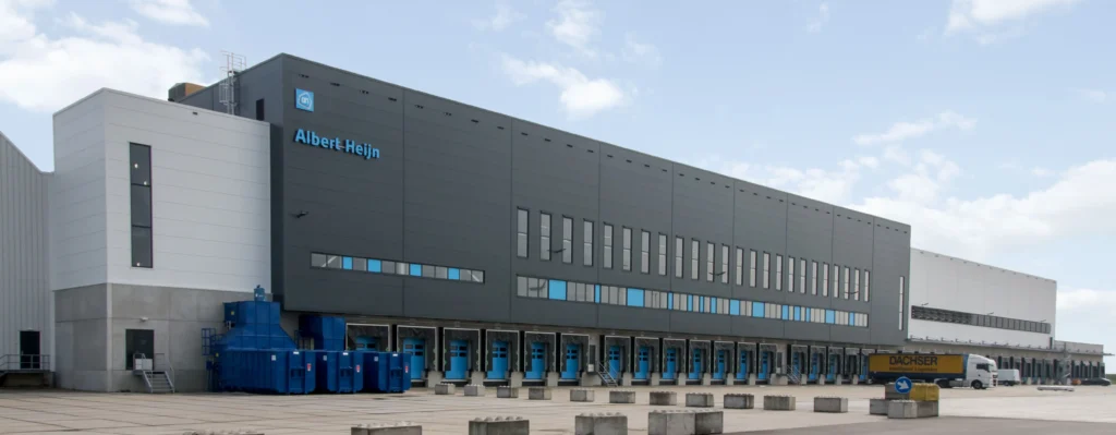 A large Albert Heijn distribution center with loading docks and a parked Dachser truck.