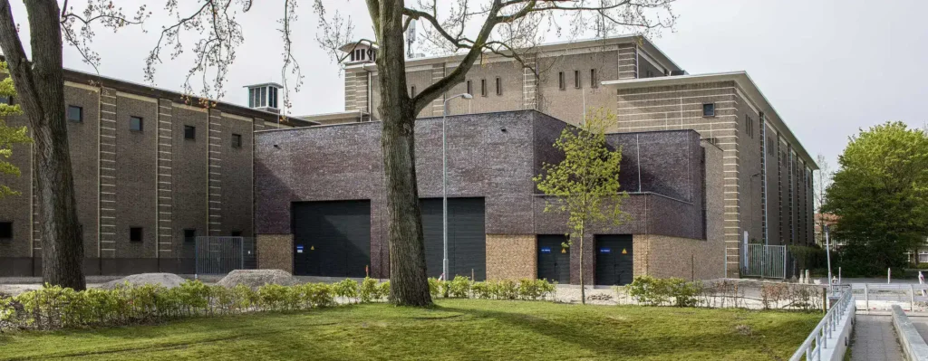 A large, modern brick building with multiple garage doors and a surrounding green landscape.