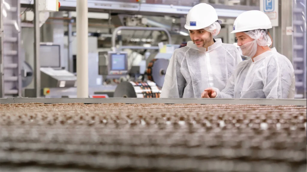 Two workers in protective clothing and helmets observe a production line at a Mars factory in Veghel.