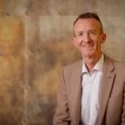 Een man in een bruin pak poseert voor een artistieke achtergrond.