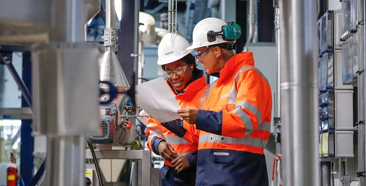 Two engineers in safety gear review project plans at an industrial site.