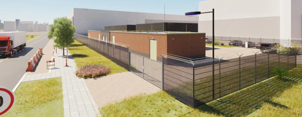 A red truck drives past a fenced brick building on a sunny day.