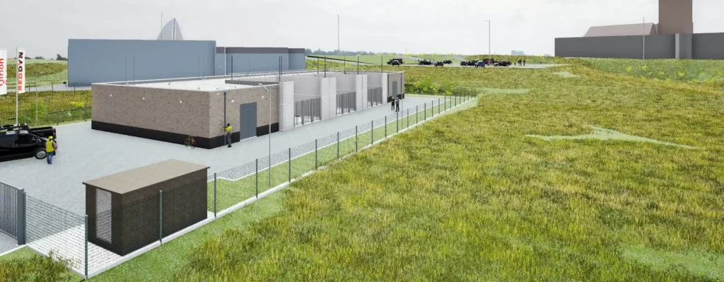 A fenced industrial facility with surrounding green fields and parked vehicles.