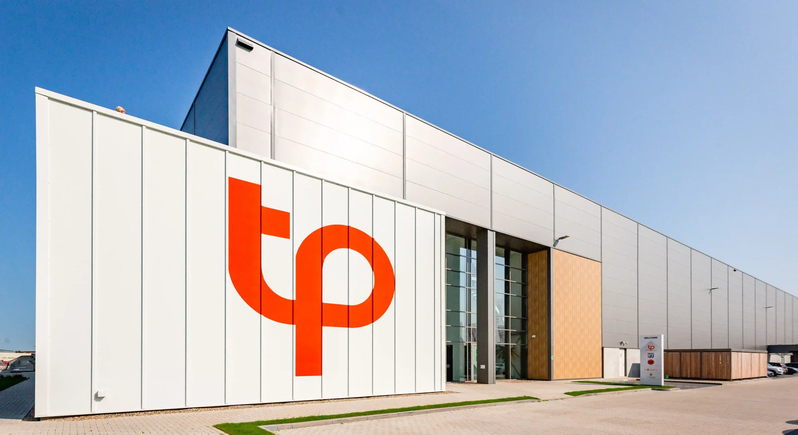 Modern industrial building with large "tp" logo on the facade under a clear blue sky.
