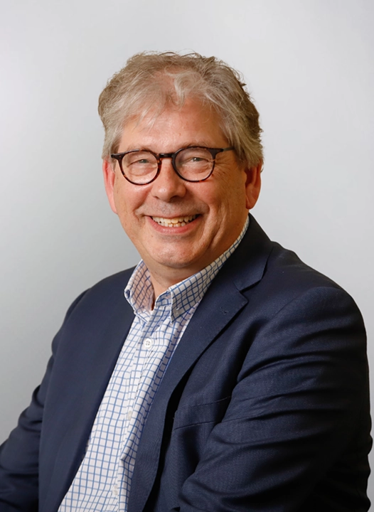 A smiling man in glasses and a suit poses for a professional portrait.