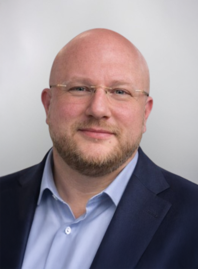 Een man met een bril en een blauwe blazer glimlacht naar de camera.
