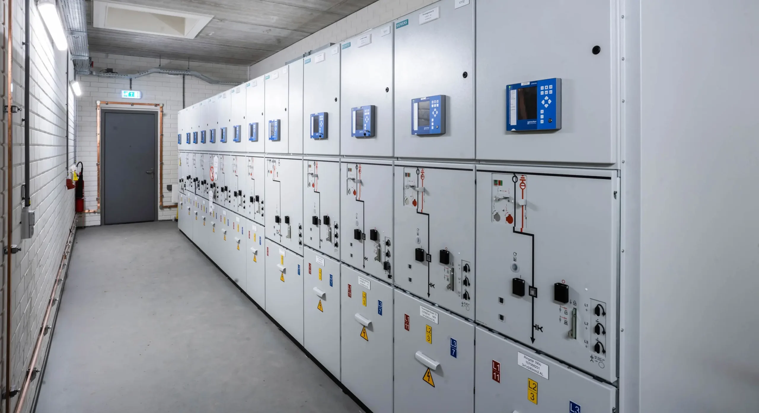 A row of electrical panels in a utility room with a grey door at the end.