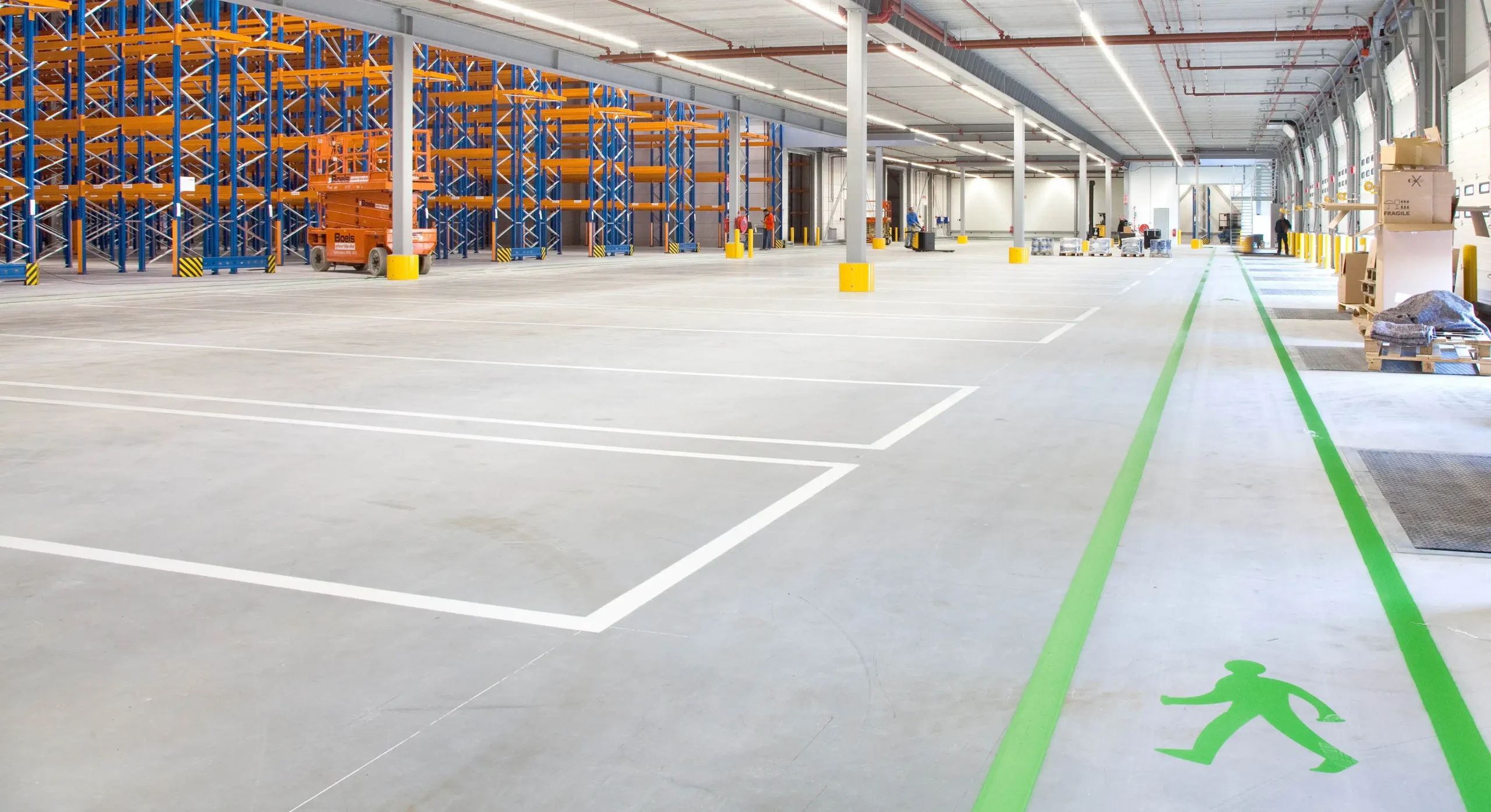 Ruime opslagplaats met lege parkeerplaatsen, stellingen en een gemarkeerd voetpad.