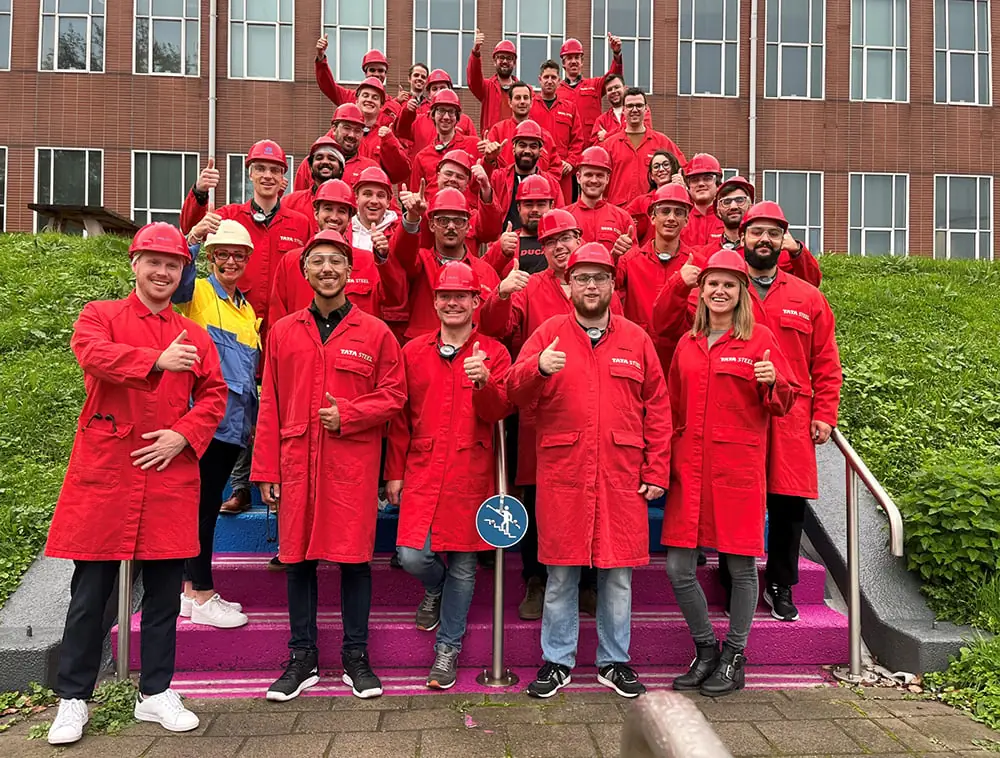 Groepsfoto van mensen in rode Tata Steel-werkkleding op een trap.