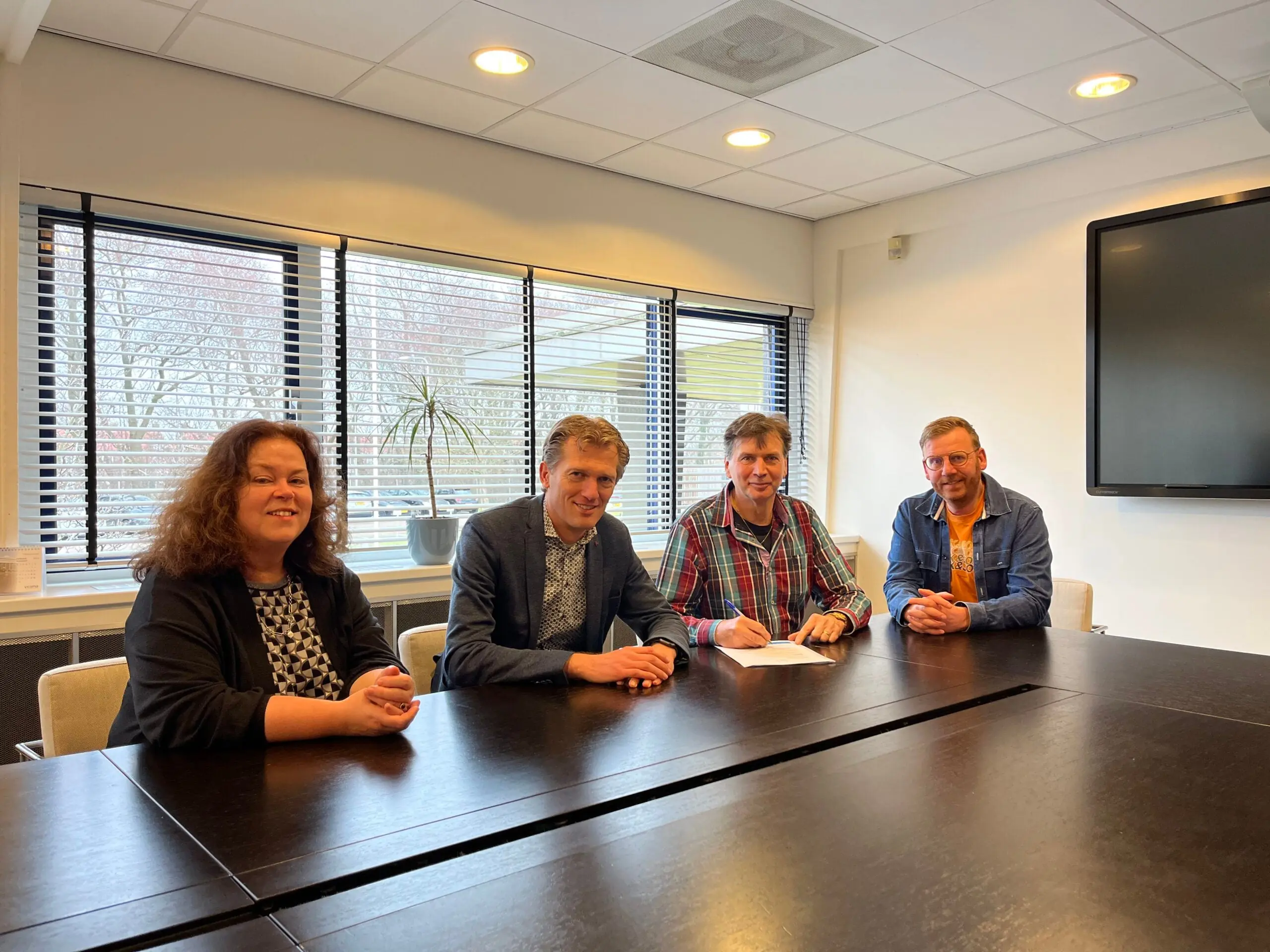 Vier mensen zitten aan een vergadertafel in een kantooromgeving.