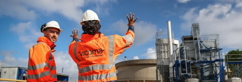 Two people wearing Vicoma-branded safety gear and helmets at an industrial site.